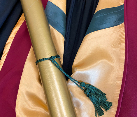 Close up of diploma rolled with green string on top of yellow, red and black graduation gown